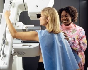 Woman Receives Mammogram.
An African-American female technician positions a Caucasian woman at an imaging machine to receive a mammogram.
Creator:	Rhoda Baer